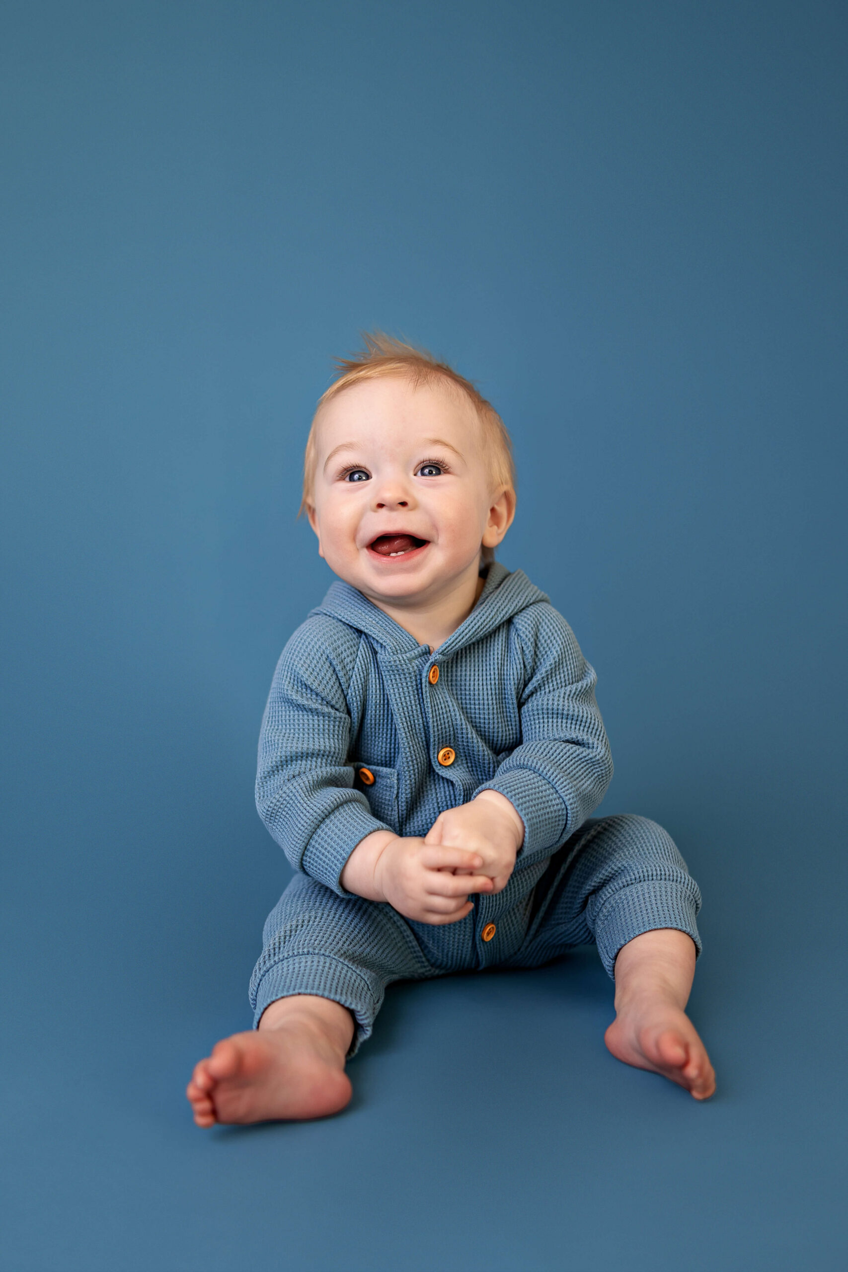 A smiling baby boy in blue jumpsuit sitting in a matching studio