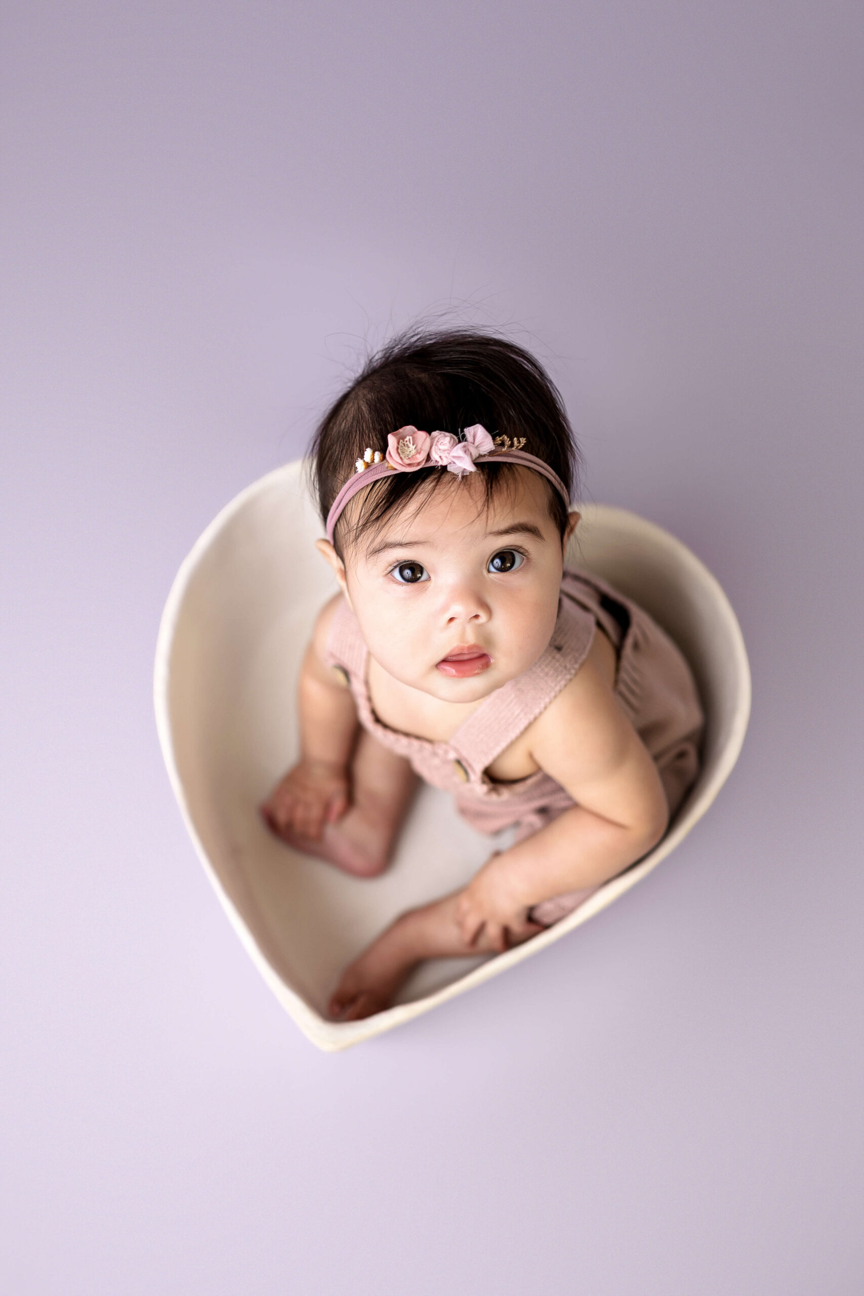A look down at an infant sitting in a heart shaped bowl in purple overalls before visiting the Normal Public Library